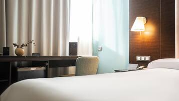 Habitación de hotel con cama, escritorio, silla, lámpara y ventana con cortinas.