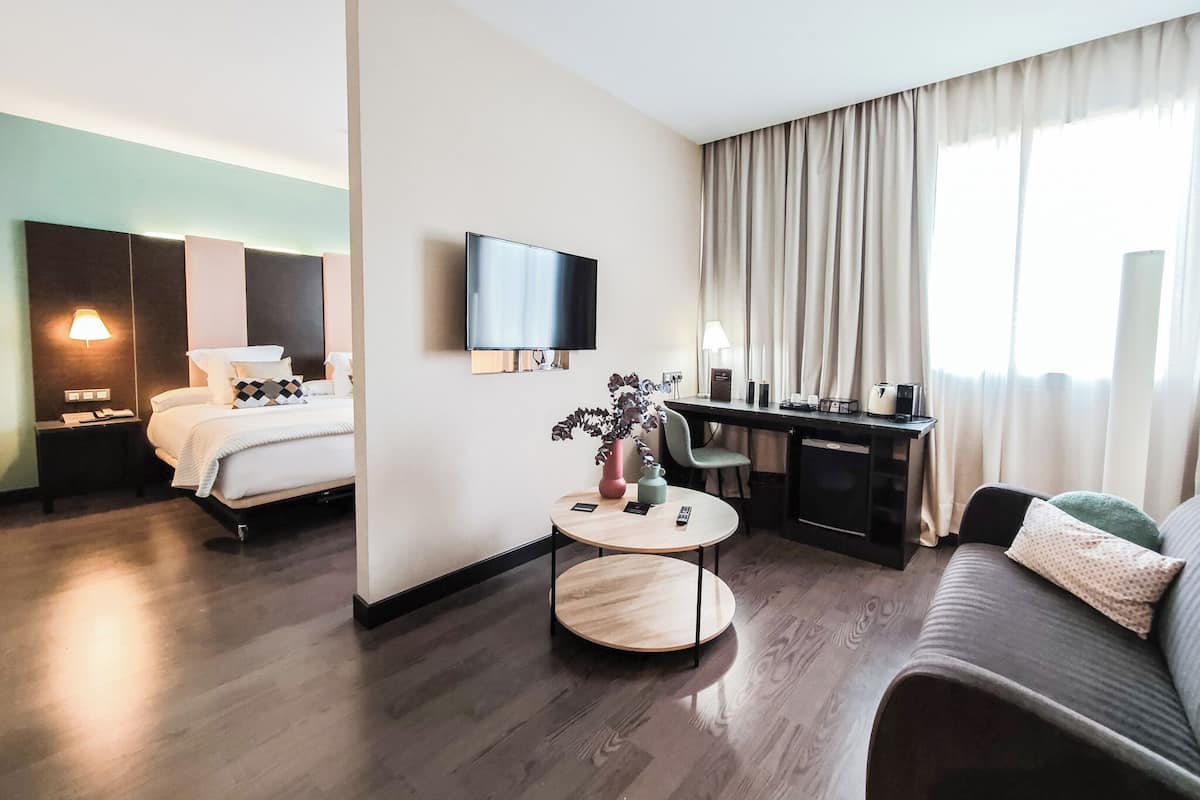 A hotel room with a bed, a desk, a sofa, a TV, and a window with curtains.