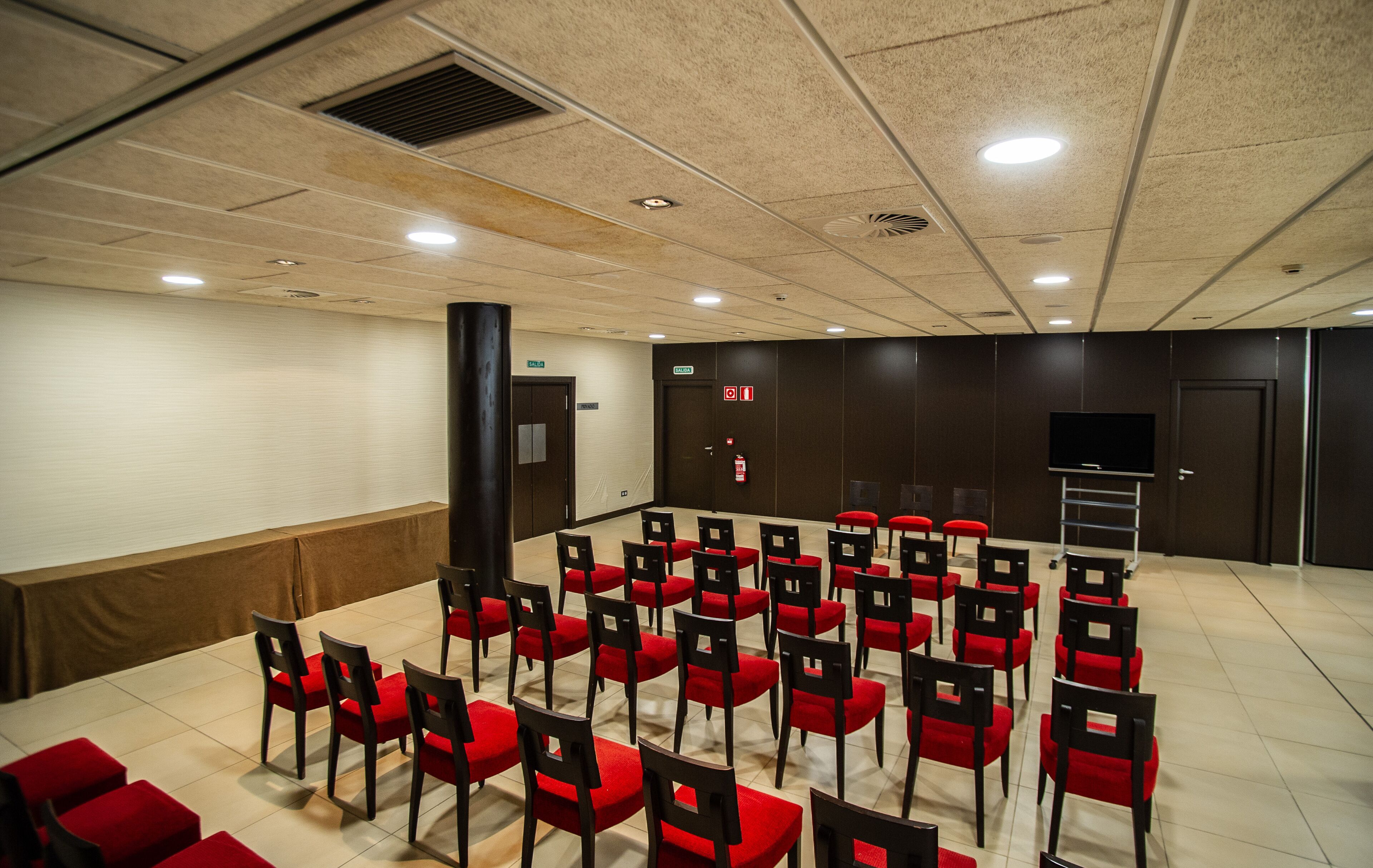 Una sala conferenze con file di sedie rosse, un podio e un grande schermo.