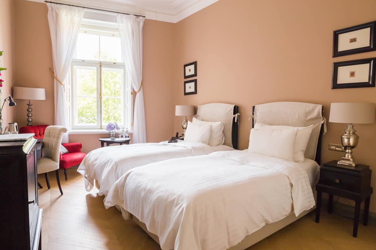 A hotel room with two beds, a desk, a chair, and a window with curtains.