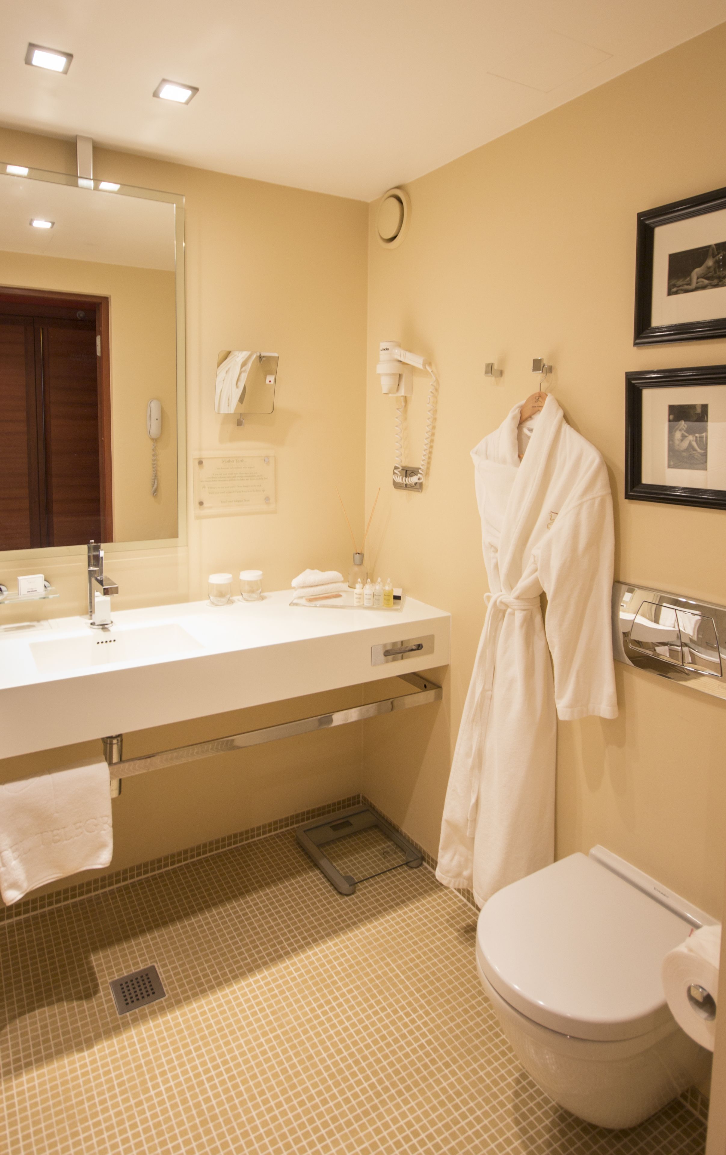 Ein Badezimmer mit einem großen Spiegel, einem Waschbecken, einer Toilette und einem an der Wand hängenden Bademantel.
