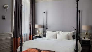 Una cama con dosel, ropa de cama blanca, dos mesitas de noche con lámparas y un banco rojo con cojines.