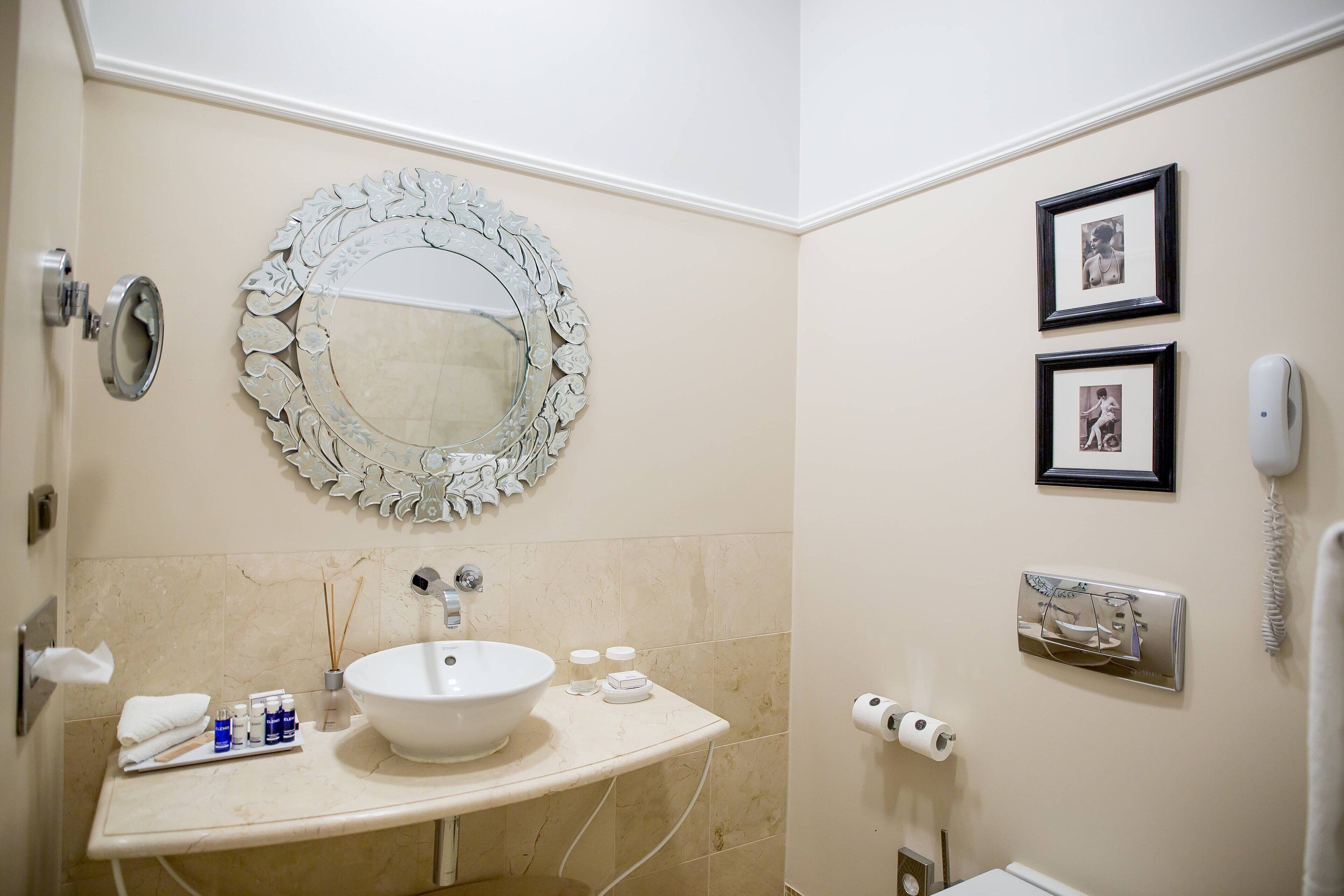A bathroom with a round mirror, sink, and two framed pictures on the wall.