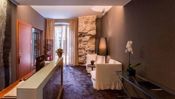 A modern hotel lobby with a reception desk, a seating area with a white sofa and armchair, a stone accent wall, and a glass coffee table.