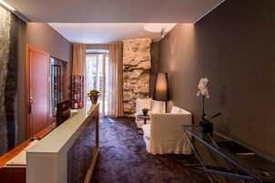 A modern hotel lobby with a reception desk, a seating area with a white sofa and armchair, a stone accent wall, and a glass coffee table.