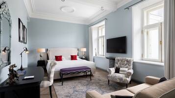 A spacious bedroom with a large bed, a flat-screen TV, a desk with a lamp, a chair, and a sofa.