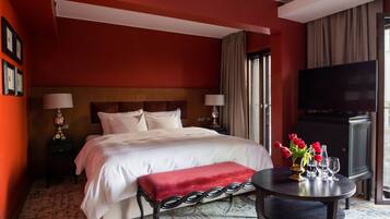 A hotel room with a large bed, a small round table with a vase of flowers, a television, and a window with curtains.
