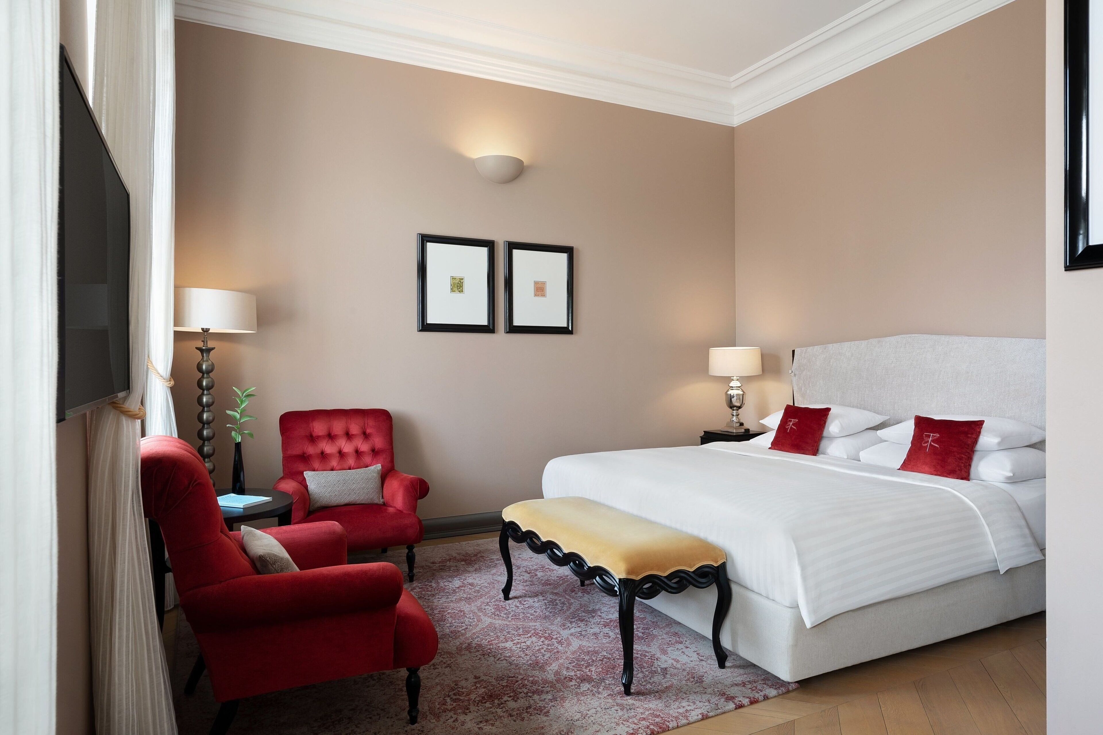 Una habitación de hotel con una cama grande, un sillón rojo, una mesita y dos cuadros en la pared.
