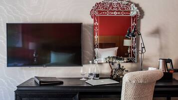 A hotel room with a flat-screen TV, a desk with a laptop, a mirror, and a chair.