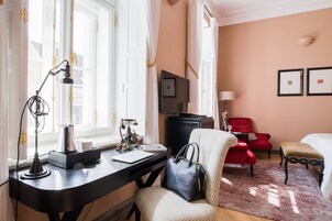 Habitación de hotel con escritorio, un sillón rojo, un sillón blanco, cama y televisión.