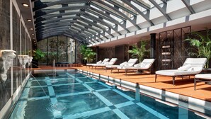 A modern indoor swimming pool with lounge chairs and a glass ceiling. - Hotel Telegraaf, Autograph Collection (Tallinn)