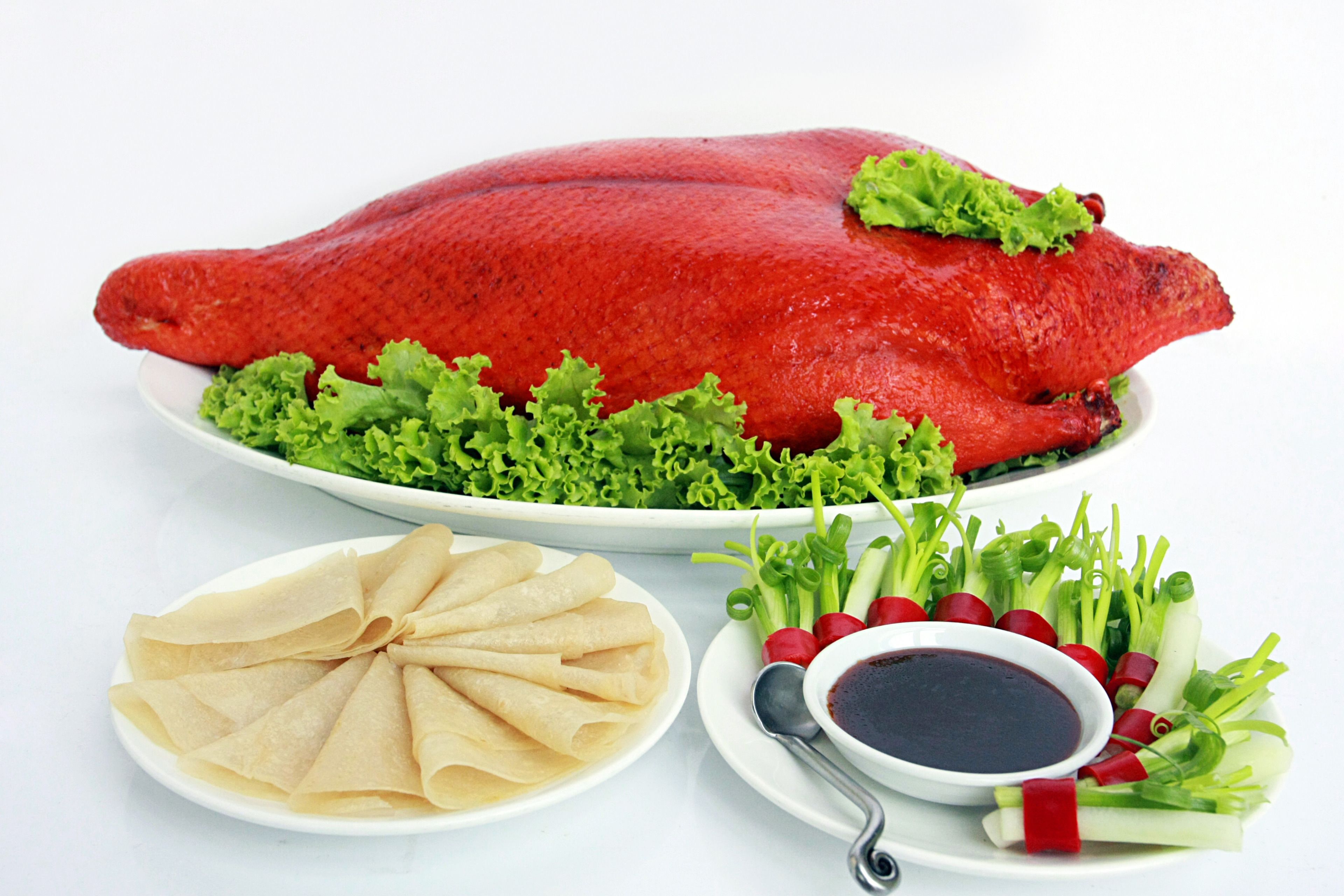 A large red roasted duck, green lettuce, and a plate of thin pancakes with a dipping sauce and sliced radishes.