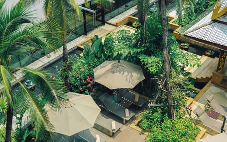 An aerial view of a resort with outdoor seating areas, palm trees, and lush greenery.
