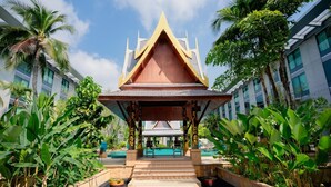 A traditional Thai pavilion with a tiled roof, surrounded by lush greenery and a swimming pool.
