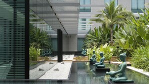 A modern indoor garden with a water feature, seating areas, and tropical plants.