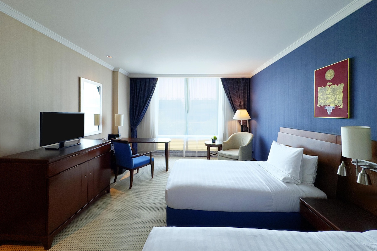A hotel room with a bed, a desk, a chair, a television, and a window with curtains.