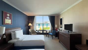 A hotel room with two beds, a desk, a TV, and a window with a view of buildings.