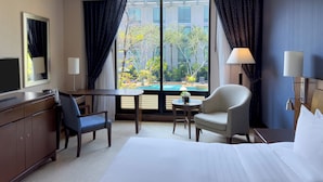 Una camera d'hotel con un letto, una scrivania, una sedia, una TV e vista su una piscina e alberi.