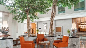 A lobby with marble flooring, orange chairs, a central table, and a large tree.