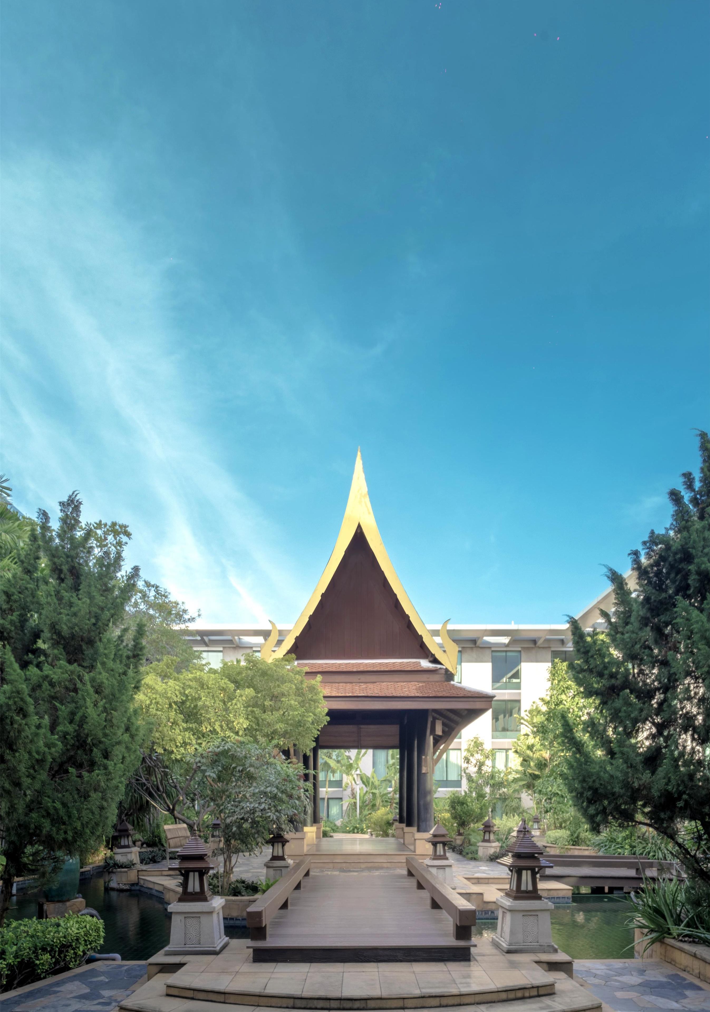 Ein traditioneller thailändischer Pavillon mit spitzer Kuppel, umgeben von üppigem Grün und blauem Himmel.