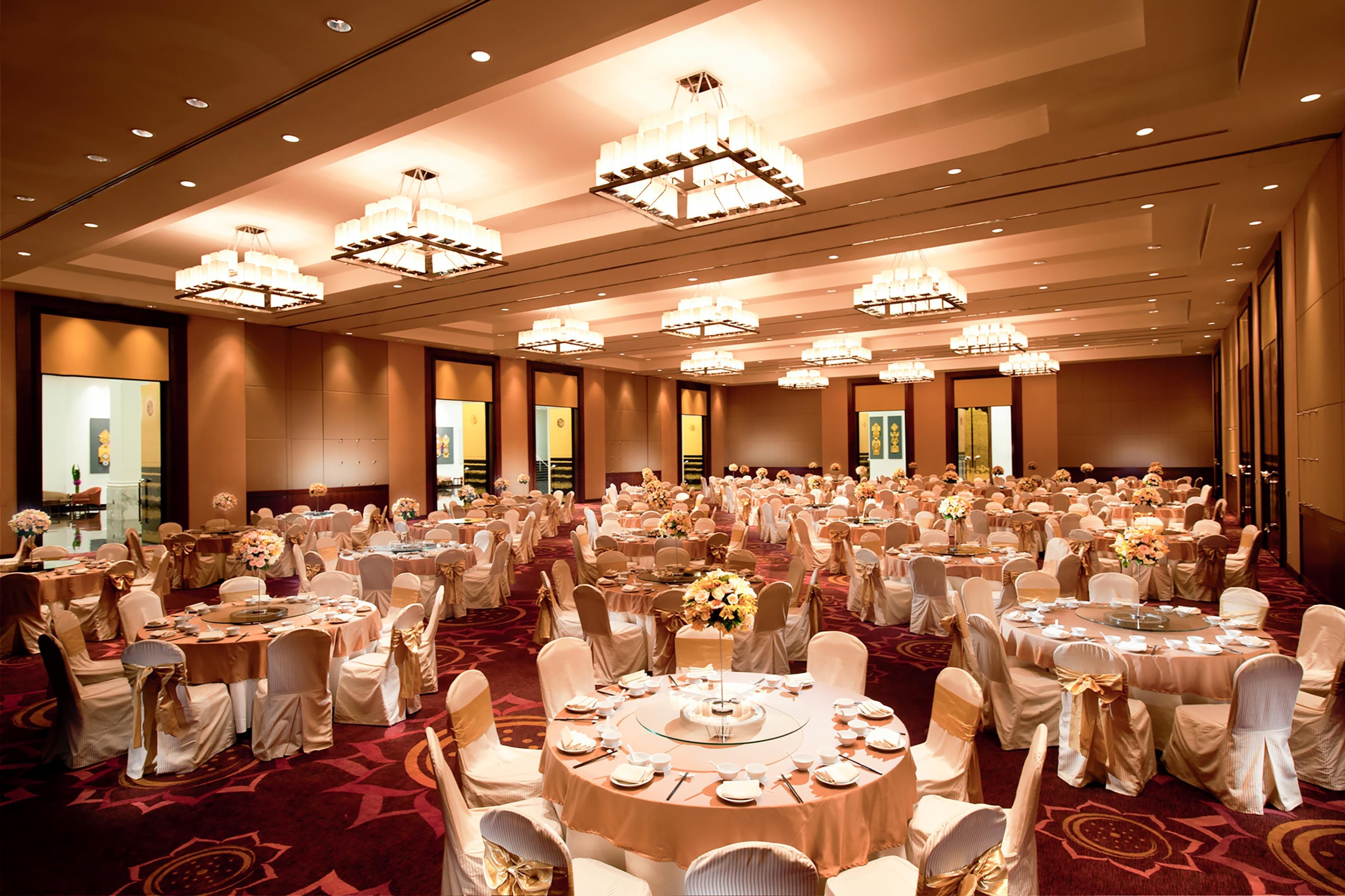 A banquet hall with round tables, chairs, and chandeliers.