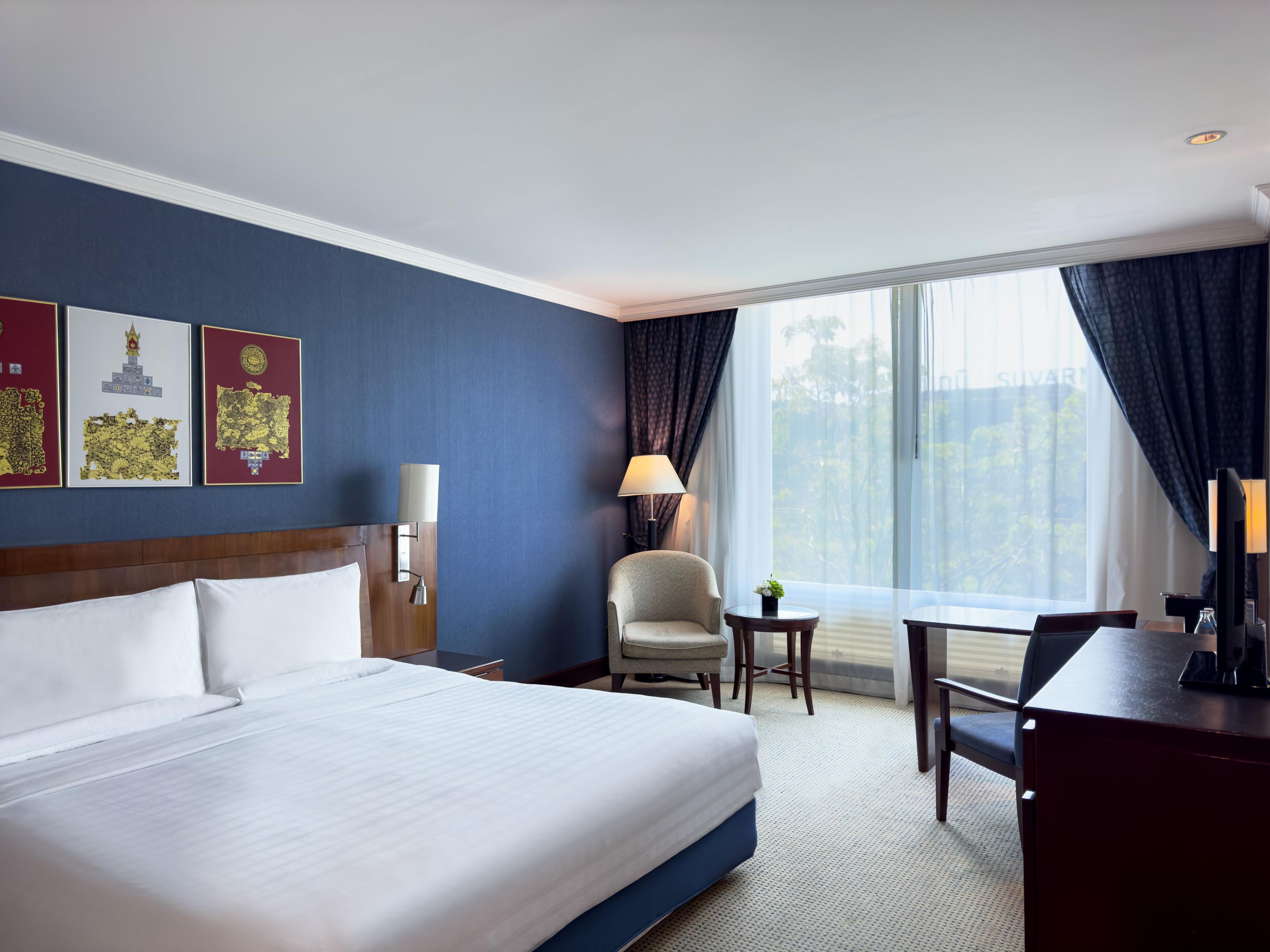 Habitación de hotel con una cama grande, un escritorio, una silla, una lámpara y una ventana con cortinas.