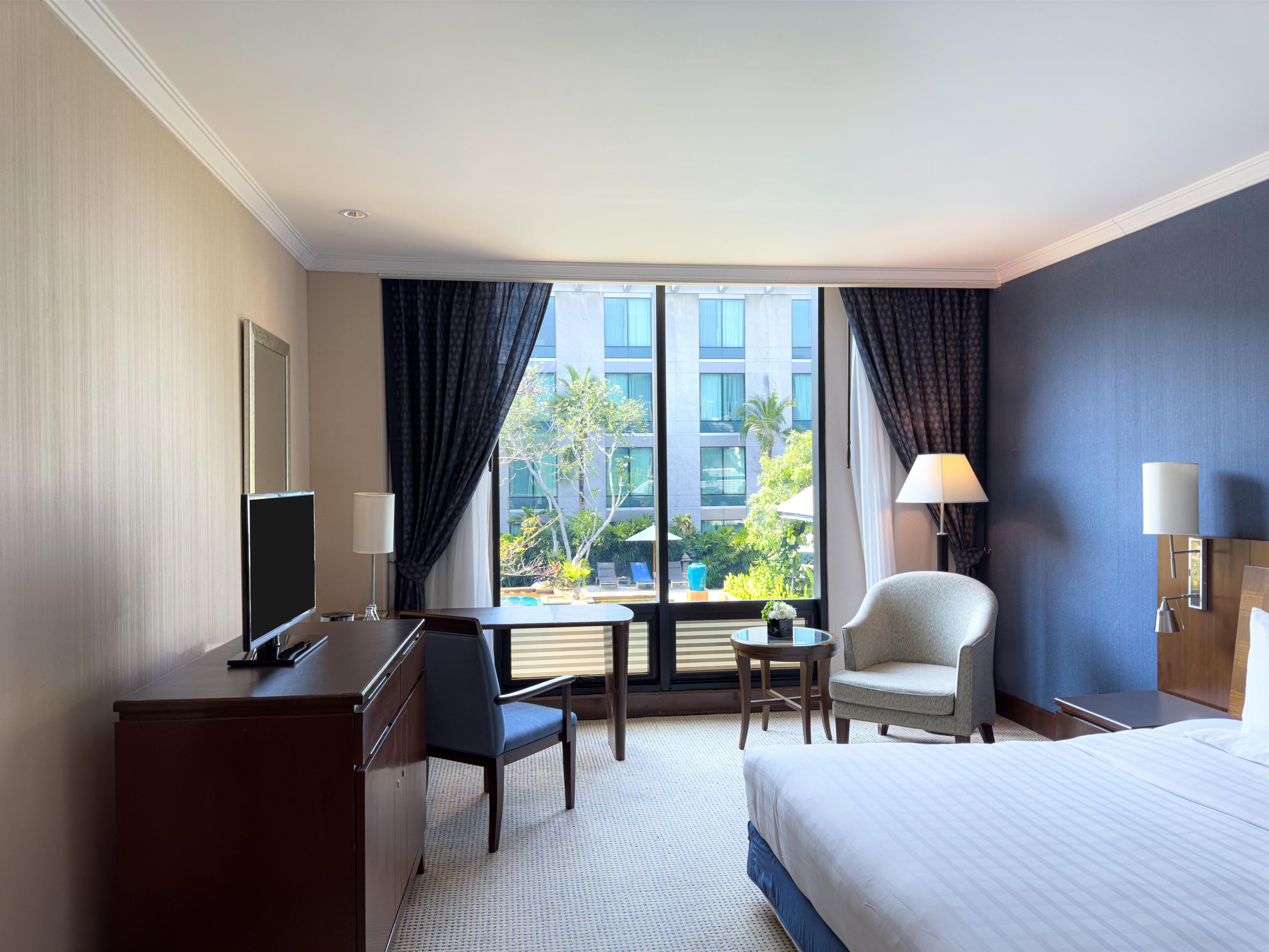 A hotel room with a bed, desk, chair, and a view of the outdoors.