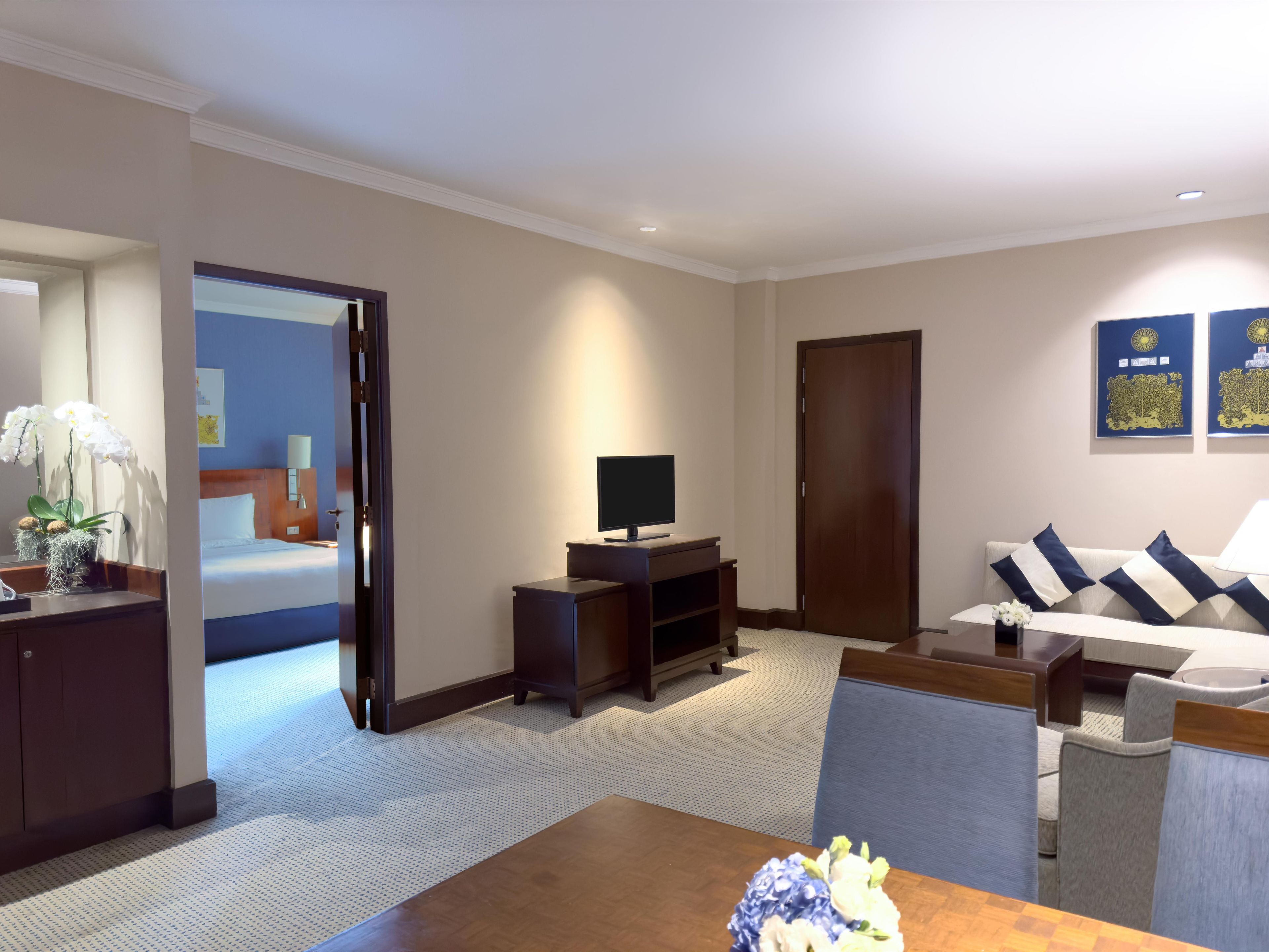 A hotel room with a bed, a TV, a desk, a sofa, and a dining table.