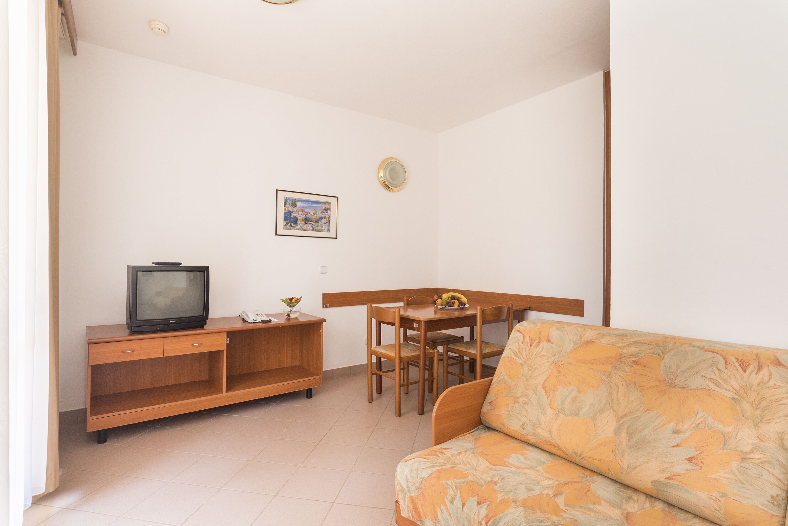 Un soggiorno con un divano, una televisione su un mobile in legno, un tavolo da pranzo con sedie e un quadro appeso al muro.