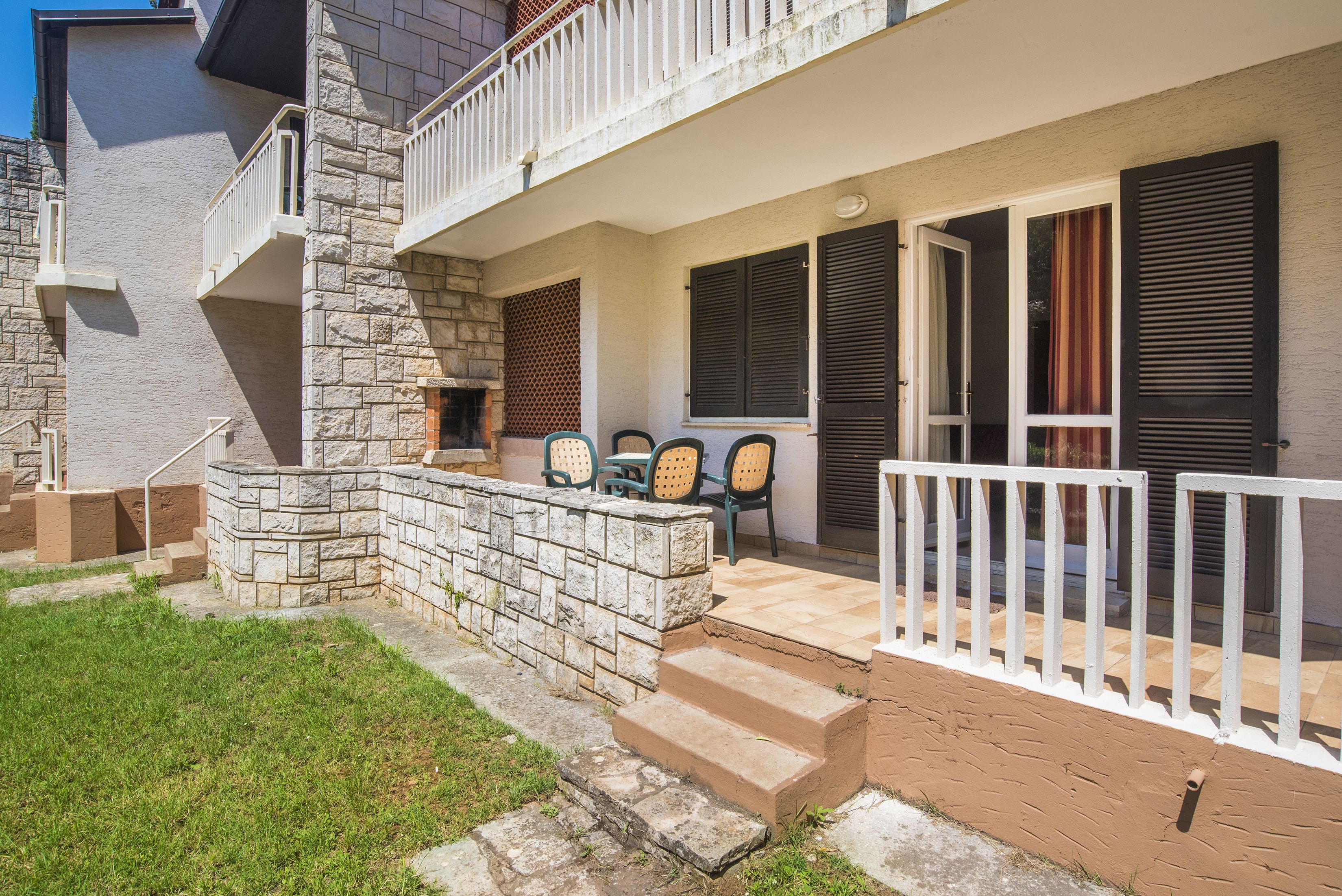 Un bâtiment à deux étages doté d’une façade en pierre, d’un balcon avec des balustrades blanches et d’un petit espace extérieur aménagé avec des chaises.