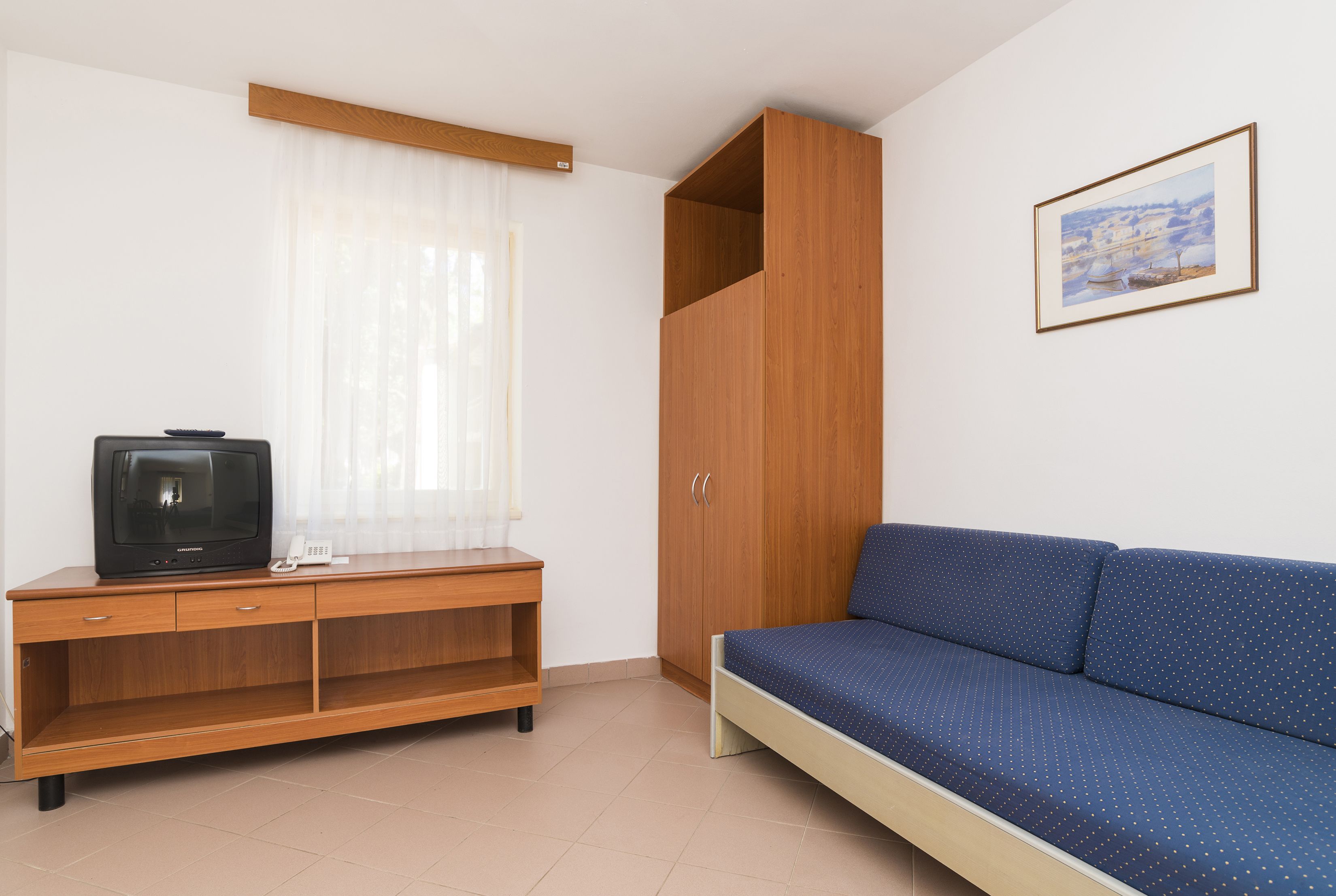 Une pièce avec un meuble en bois, un canapé bleu, un tableau accroché au mur et un téléviseur posé sur le meuble.