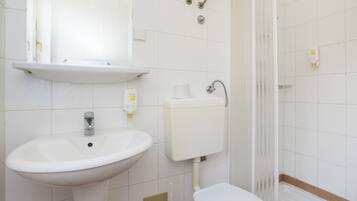 Un baño con lavamanos, inodoro y ducha blancos.