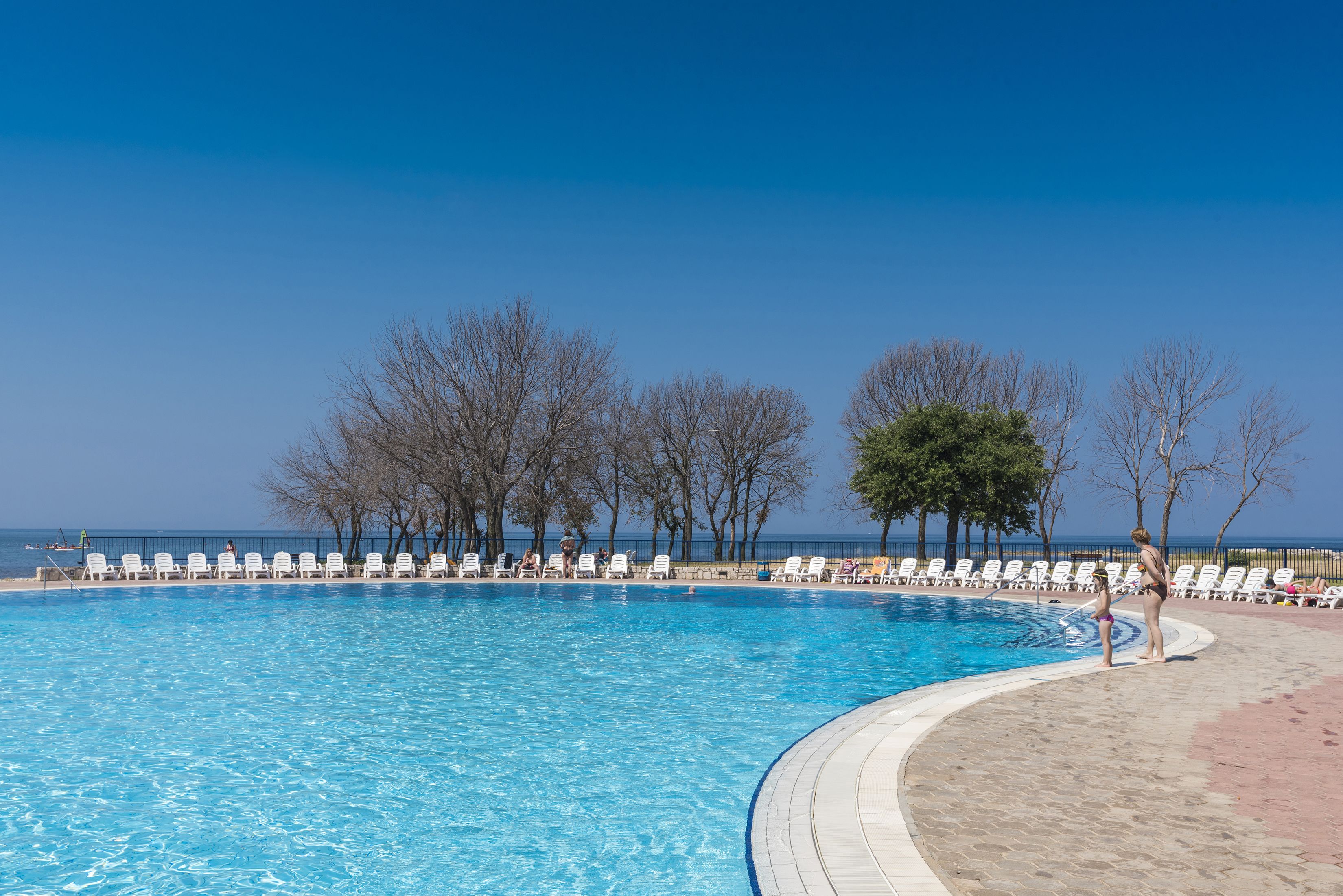Una piscina con sillones de descanso y vista al mar.