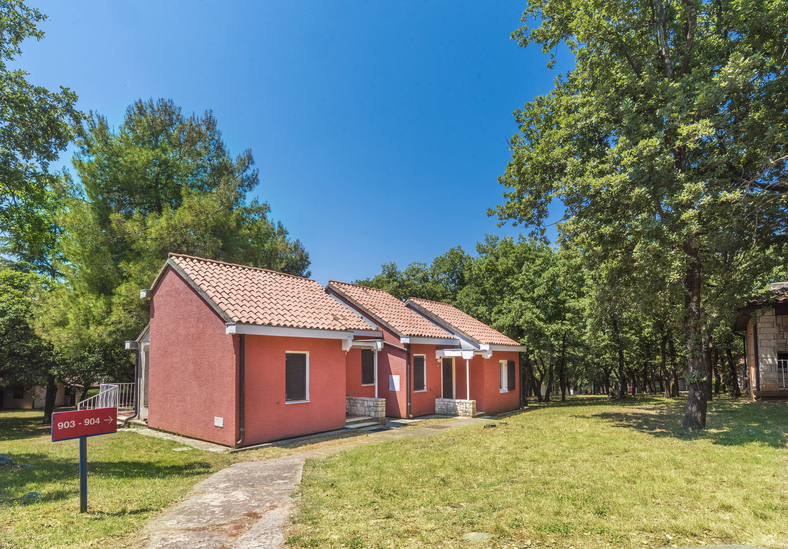 A row of red brick buildings with a tiled roof, a grassy lawn, and trees in the background.