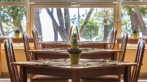Un espace repas avec des tables et des chaises en bois, des plantes en pot et une vue sur les arbres à travers de grandes fenêtres.