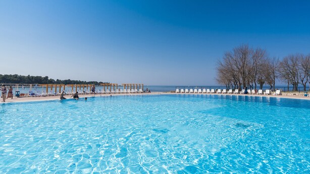 Une grande piscine d’un bleu éclatant, dotée de chaises longues et surmontée d’une pergola en bois.