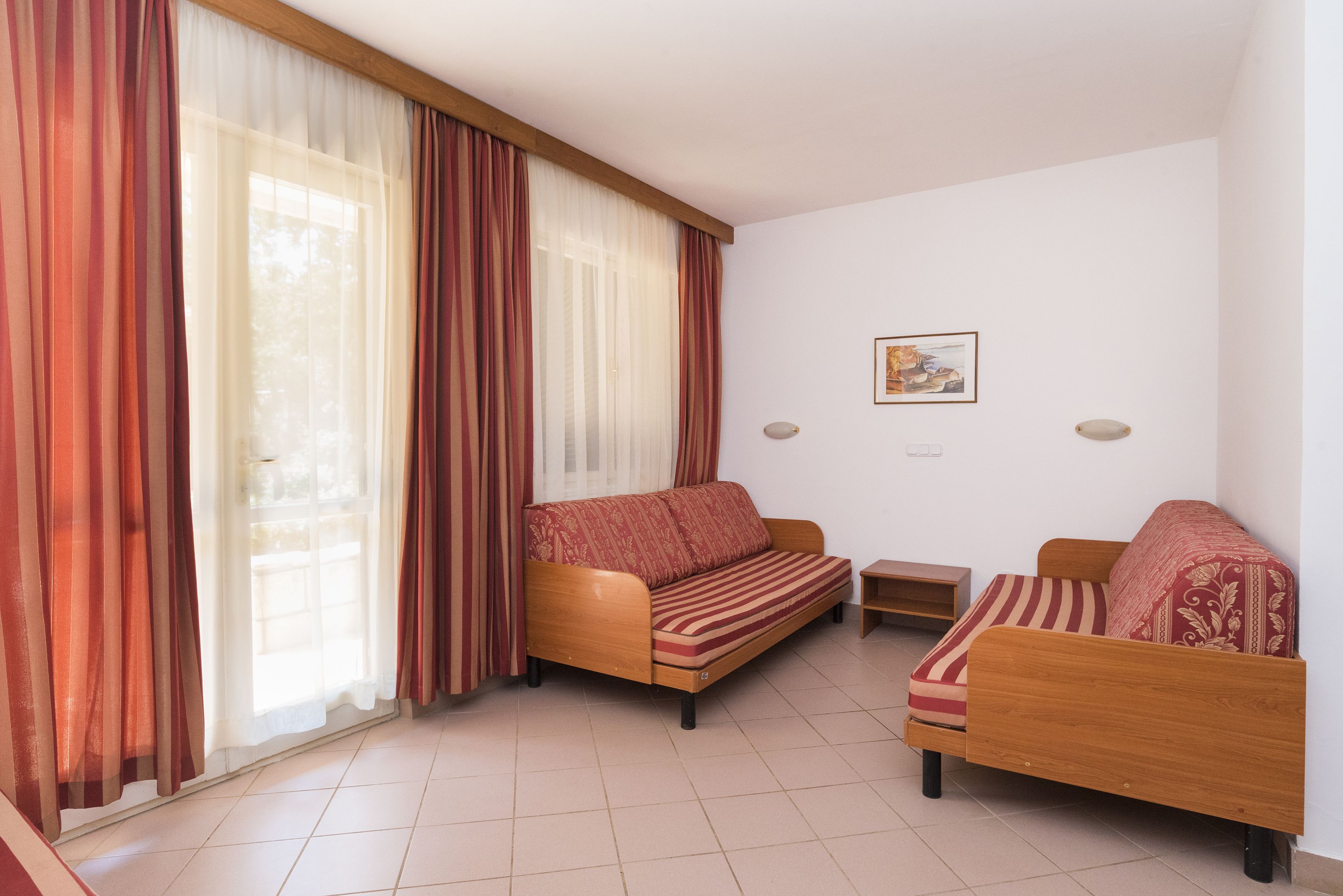 Una habitación con dos sofás de madera, una mesita y un ventanal con cortinas traslúcidas.