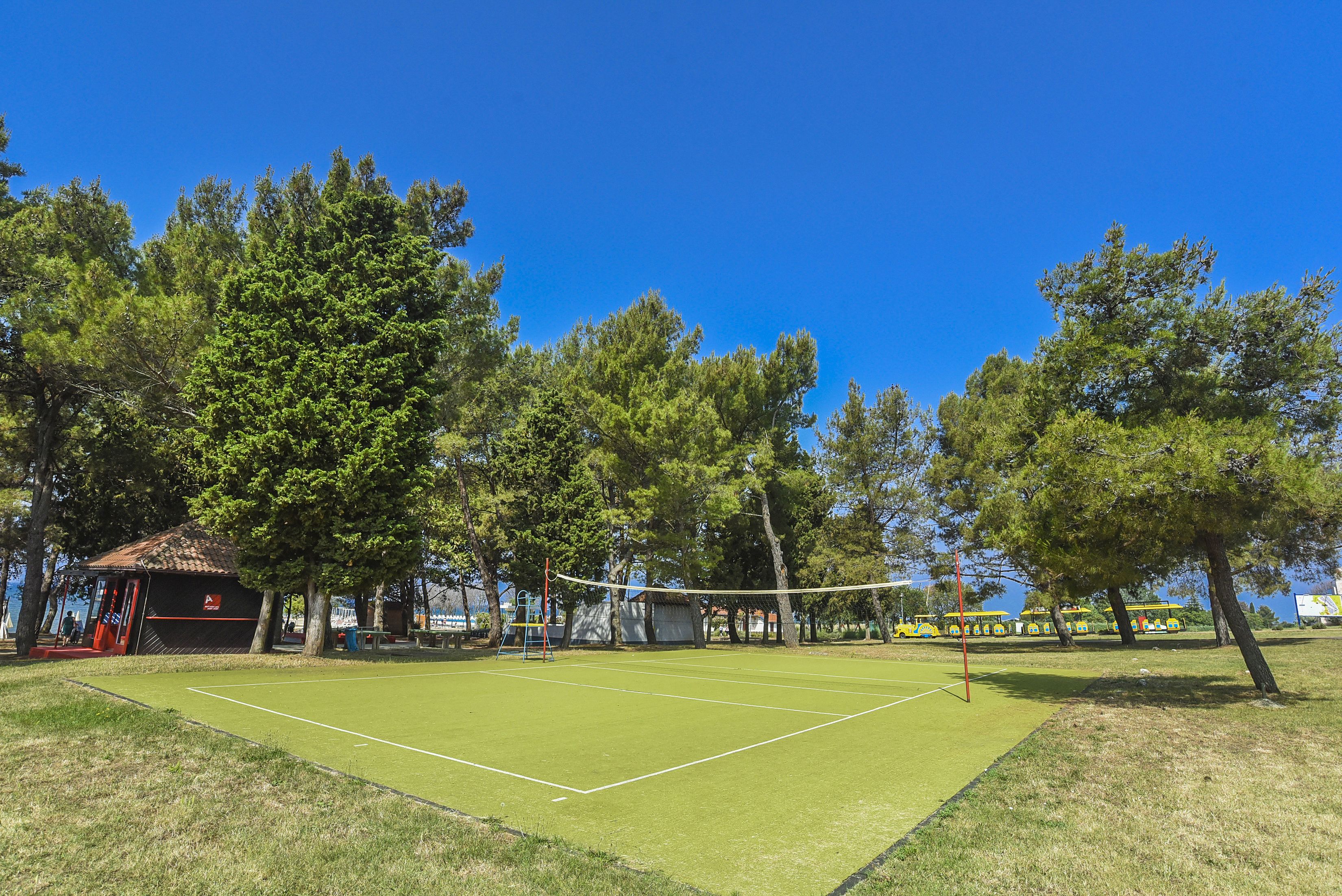 Un court de tennis avec un filet, entouré d’arbres et agrémenté d’un petit pavillon.