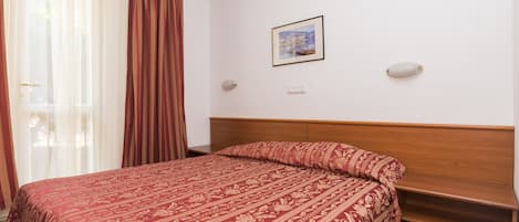 Ένα στρωμένο κρεβάτι με προσεγμένο τρόπο, με ένα διακοσμητικό κάλυμμα, ένα ξύλινο προσκέφαλο και μια κορνιζαρισμένη εικόνα στον τοίχο.
