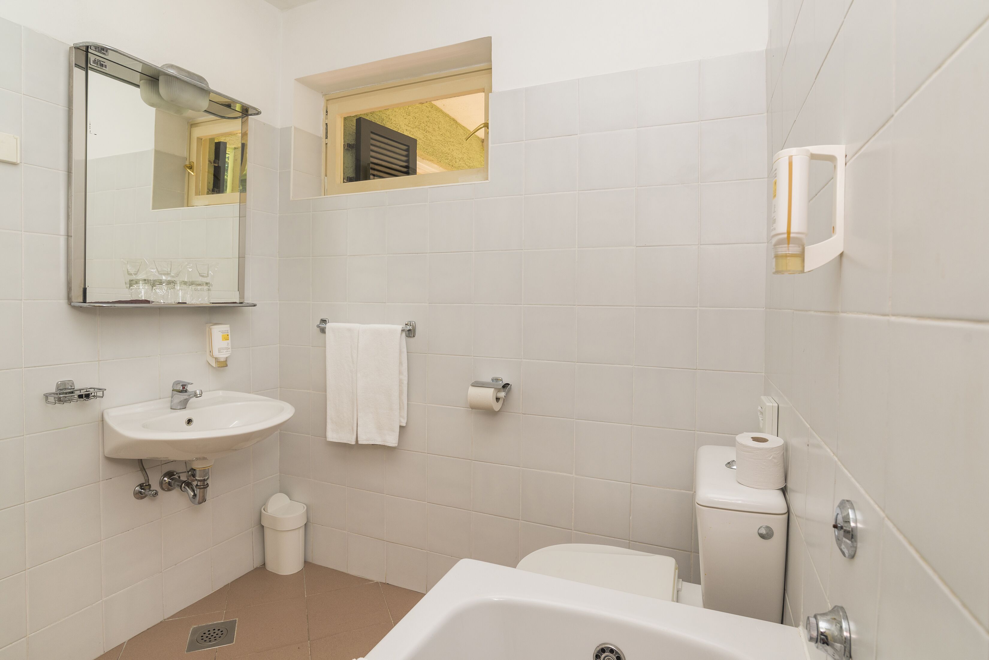 Ein Badezimmer mit Waschbecken, Spiegel, Toilette und einem kleinen Fenster.