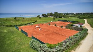 Un court de tennis avec vue sur la mer et un chemin menant à un bâtiment.