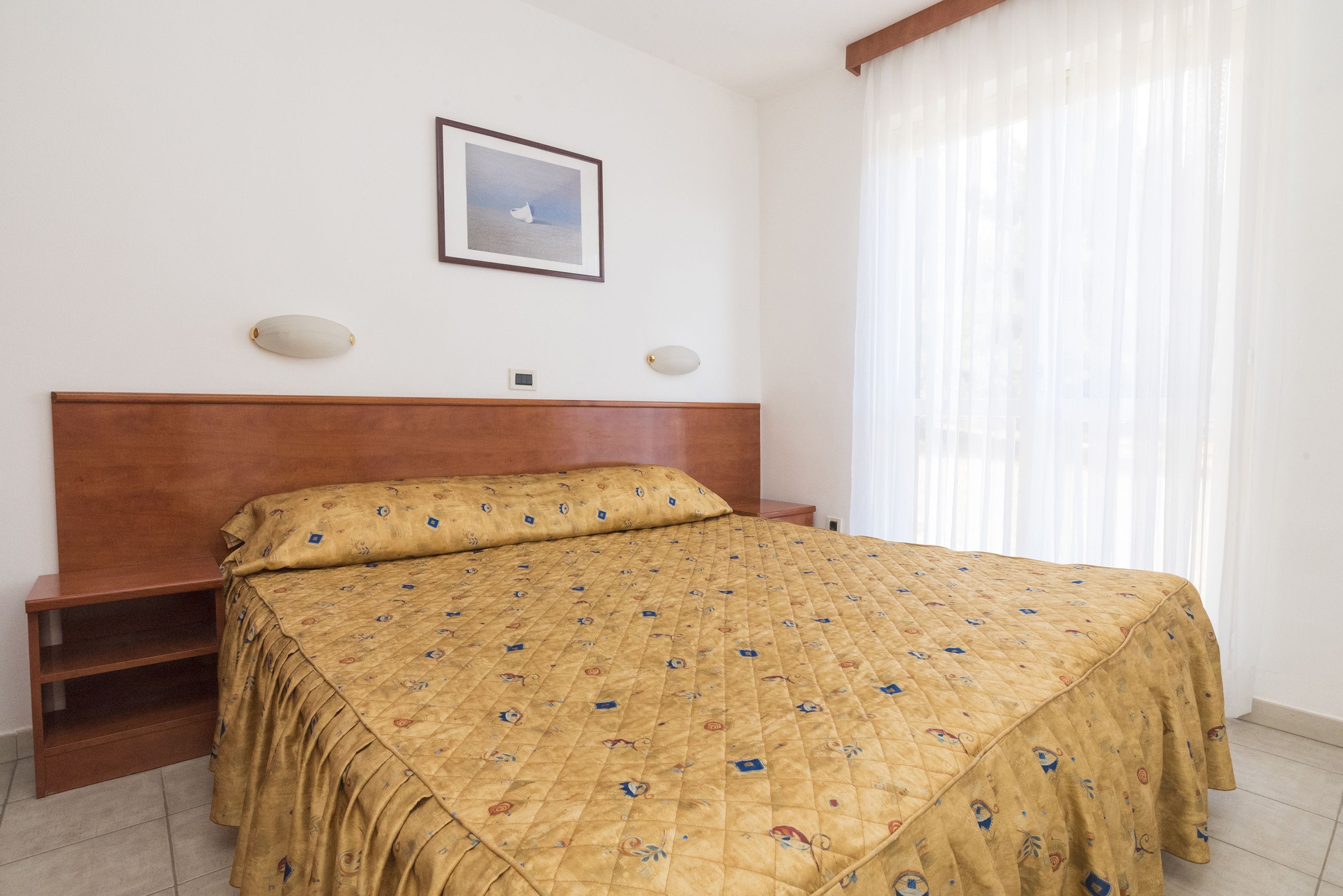 Une chambre à coucher avec une tête de lit en bois, un lit recouvert d’une couvre-lit à motifs, une table de chevet et un tableau encadré accroché au mur.