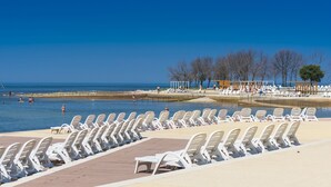 Un espace piscine situé au bord de la plage, avec des rangées de chaises longues blanches et une vue dégagée sur la mer.