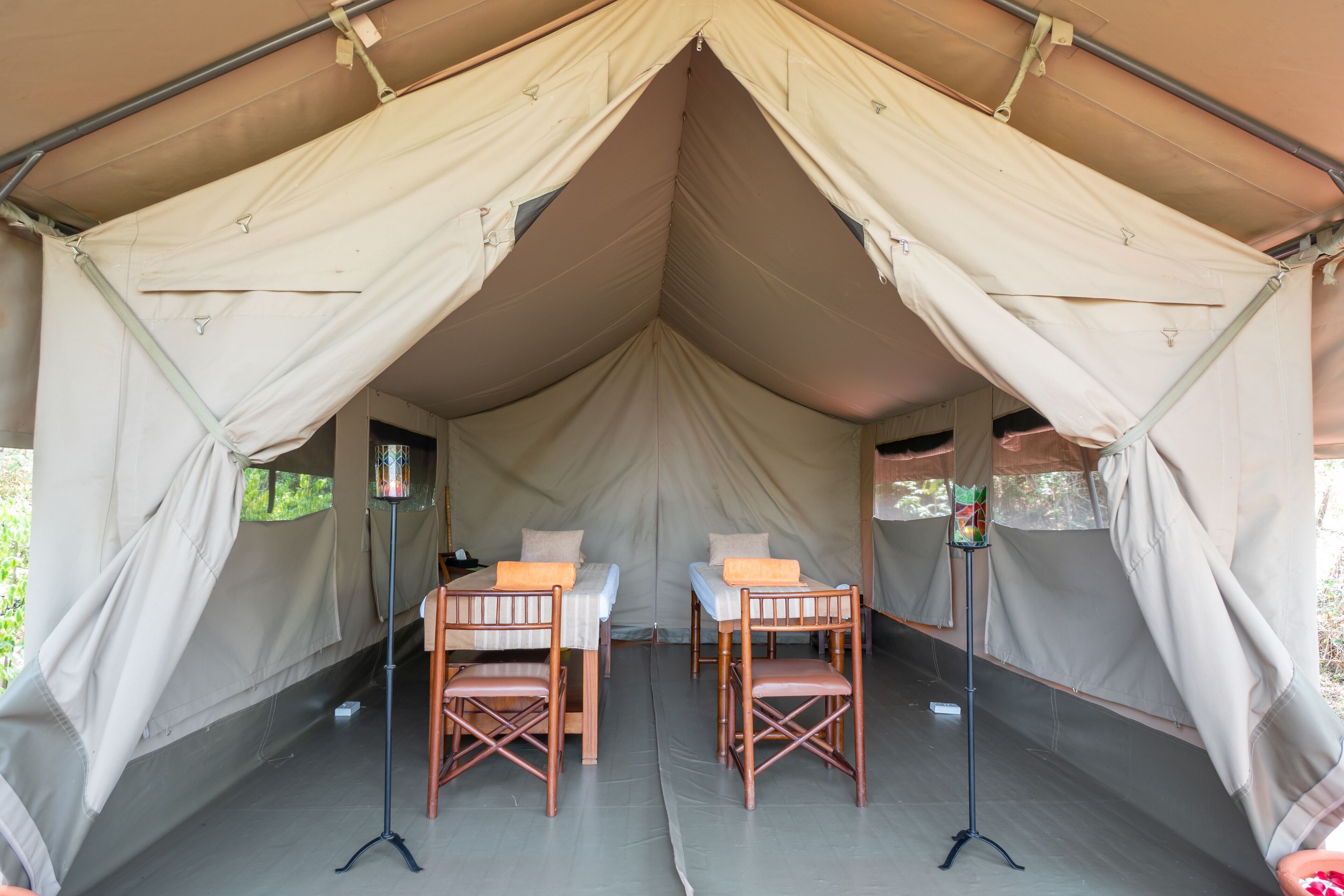 A tent with two beds, each with a wooden frame and a pillow. There are two standing lamps with lampshades.