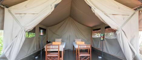 A tent with two beds, each with a wooden frame and a pillow. There are two standing lamps with lampshades.