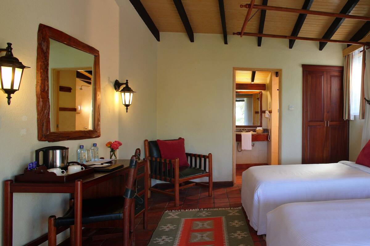 Habitación de hotel con dos camas, un escritorio con silla, un espejo y techo de madera.