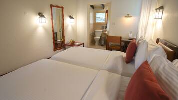 Habitación de hotel con dos camas, una mesita, una silla, un espejo y un baño visible a través de una puerta abierta.