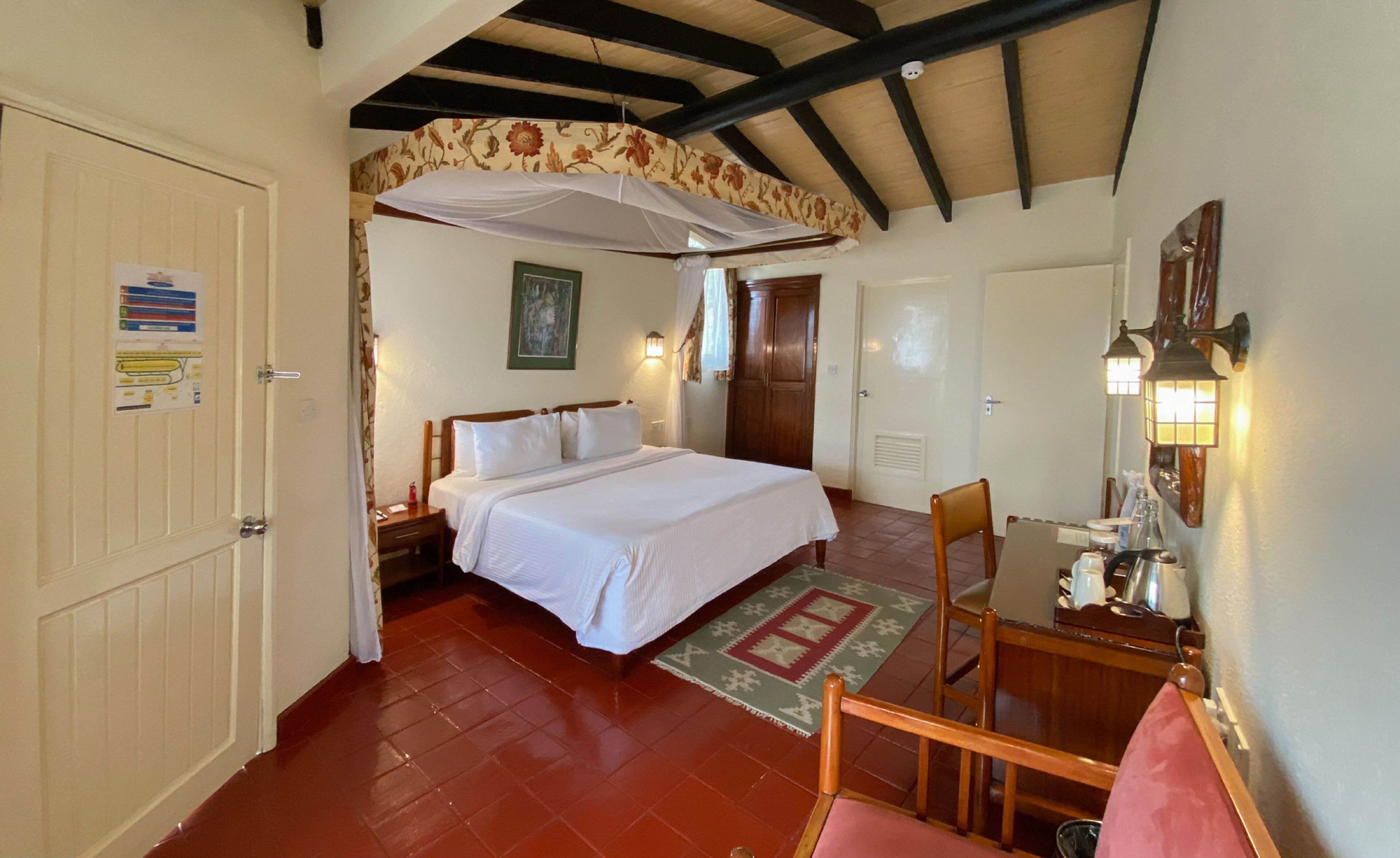 A bedroom with a bed, a nightstand, a chair, a table, a lamp, and a door.