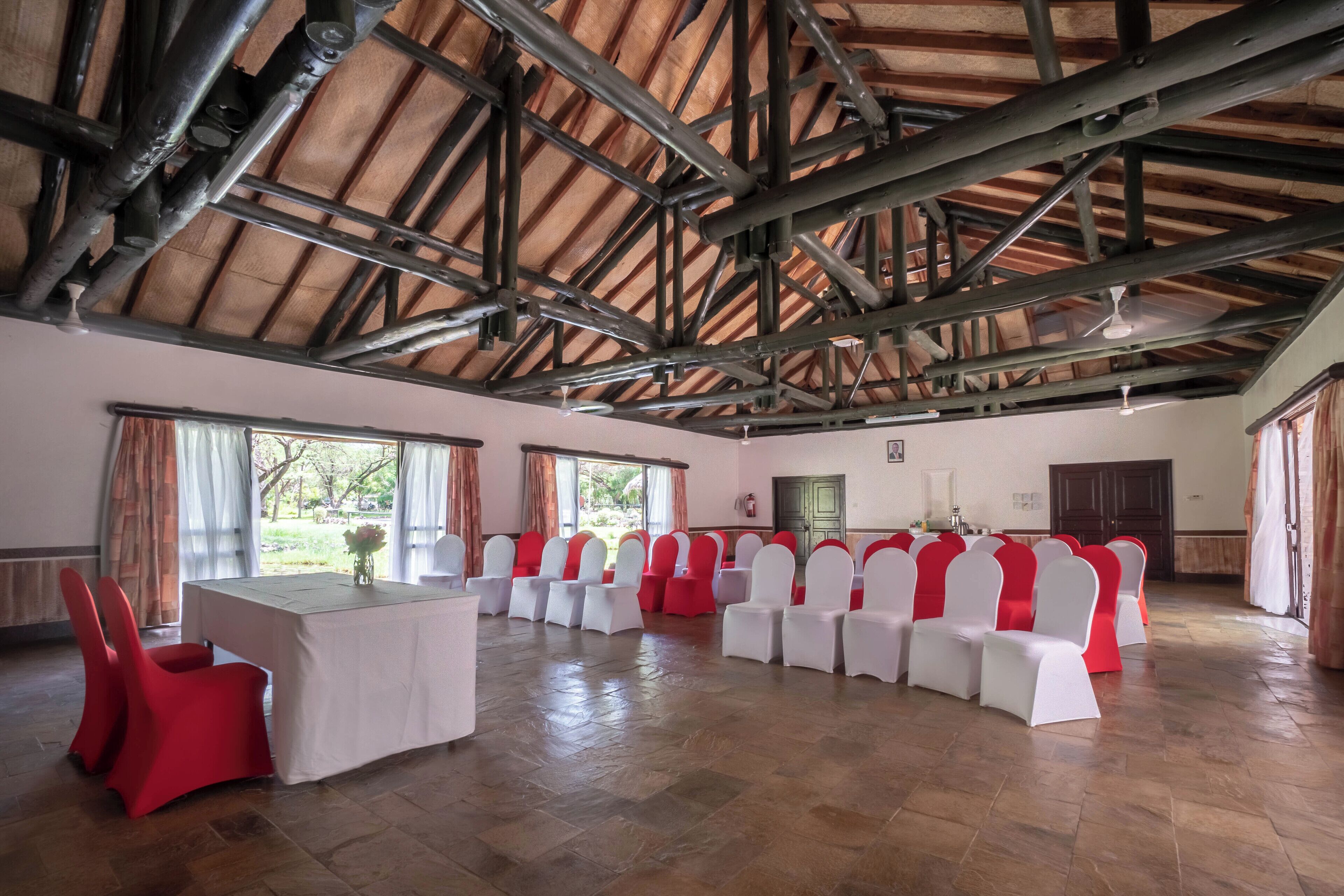 Un salón amplio con techo de madera alto y una larga mesa rodeada de filas de sillas con cubres rojos y blancos.