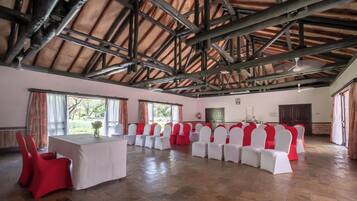 Un salón amplio con techo de madera alto y una larga mesa rodeada de filas de sillas con cubres rojos y blancos.
